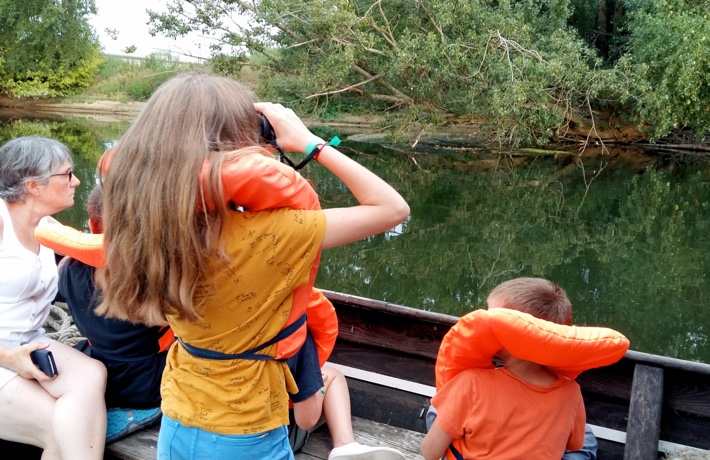 Quatre personnes dans une embarcation en bois, dont trois jeunes gens avec bouée, observent la biodiversité des bords de Loire.