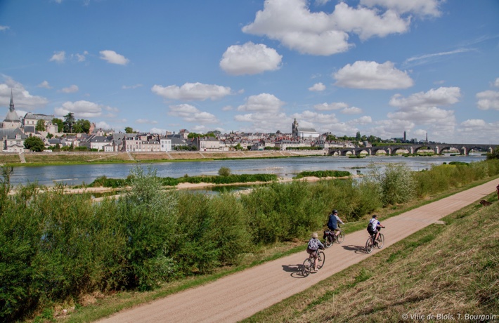 Trois cyclistes circulent sur la piste de la Loire à vélo et se dirigent vers le pont Jacques-Gabriel.