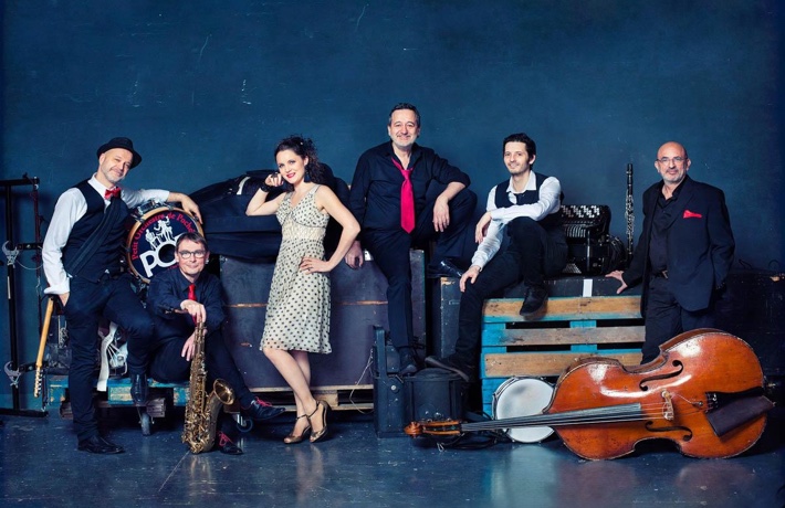 Photo du groupe « Le Grand Pop », posant avec ses instruments (guitare, saxophone, batterie, clarinette, accordéon et violoncelle) en souriant.