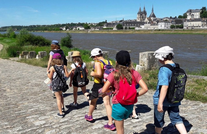 Jeunes gens emmenés par une guide le long de la Loire, avec l’église Saint-Nicolas et le Château royal en arrière-plan.