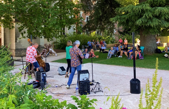 Un groupe donne un concert dans les jardins de la terrasse du Foix du Château, devant plusieurs dizaines de personnes sur l’herbe ou sur des chaises longues.
