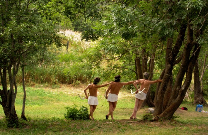 Trois hommes en sous-vêtements se tiennent contre un arbre dans la forêt, chacun avec leur arc et leur flèche.