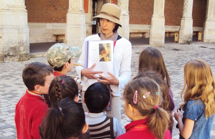 Une guide anime une visite guidée du Château face à un petit groupe d’enfants, dans la cour.