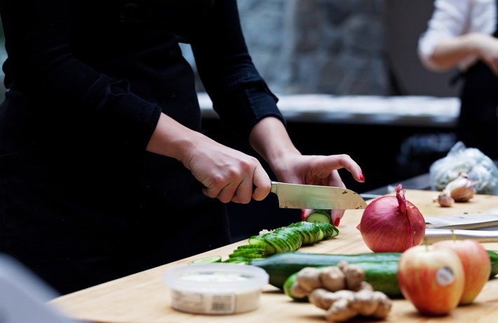 Personne coupant un concombre sur un plan de travail de cuisine, avec d’autres fruits et légumes posés à côté.