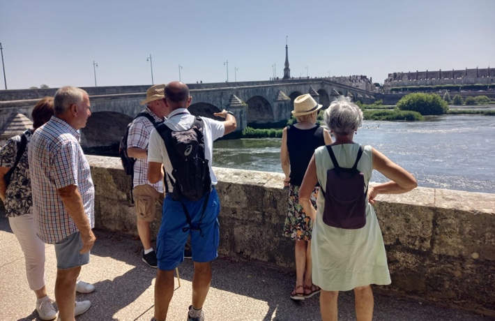 Une personne mène une visite autour de 5 autres, sur les quais, en direction du pont Jacques-Gabriel.