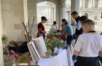 Dans la cour du Château, des personnes s’approchent d’une table, tenue par une animatrice, où sont exposés des objets de l’époque Renaissance.