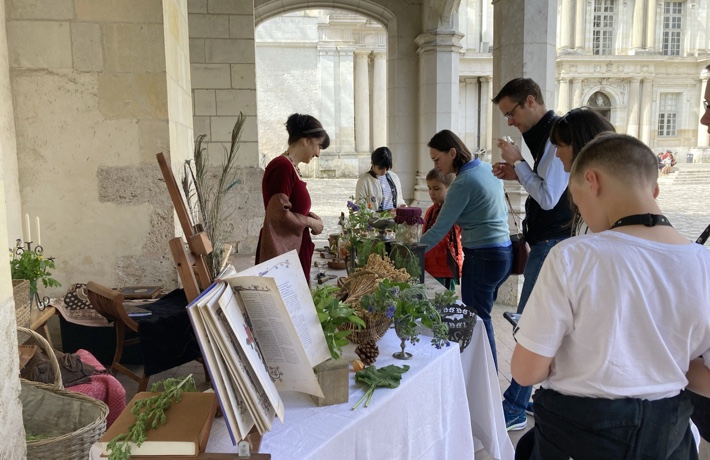 Dans la cour du Château, des personnes s’approchent d’une table, tenue par une animatrice, où sont exposés des objets de l’époque Renaissance.