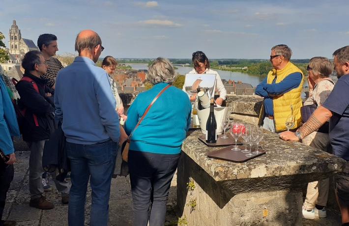 Des personnes en haut d’une tour du château écoutent une guide-conférencière présenter le patrimoine, avec des verres d’apéritifs à leurs côtés.