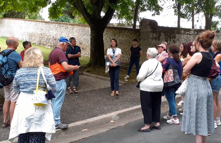 Une guide-conférencière anime une visite entourée de plus d’une dizaine de personnes.